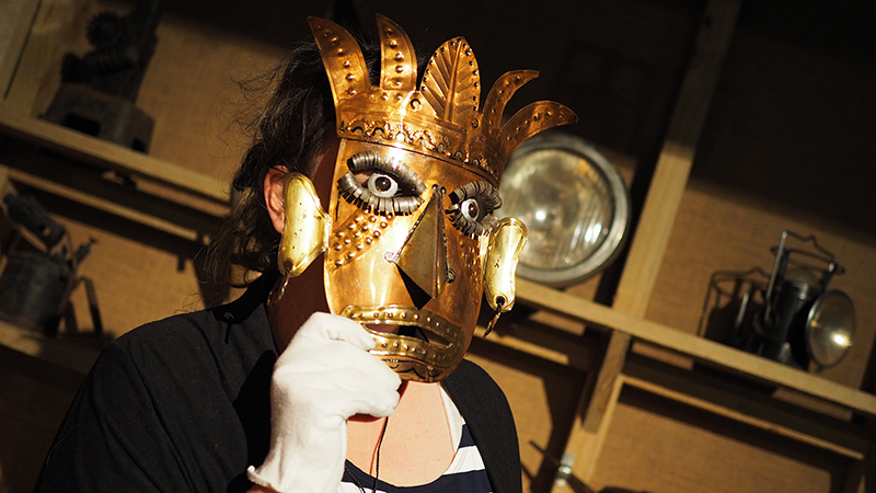 A woman wearing a brass-coloured metal mask from Mexico
