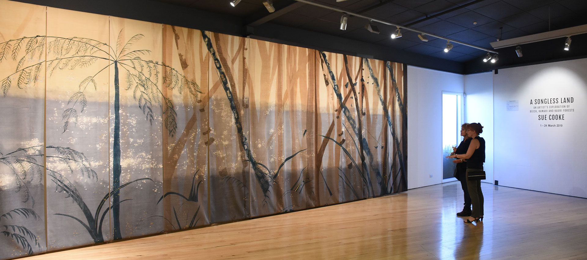 Large printed panels depicting regenerating forest stretch from floor to ceiling in an art gallery