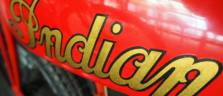 A closeup of a red motorcycle, showing the model name "Indian" in gold script
