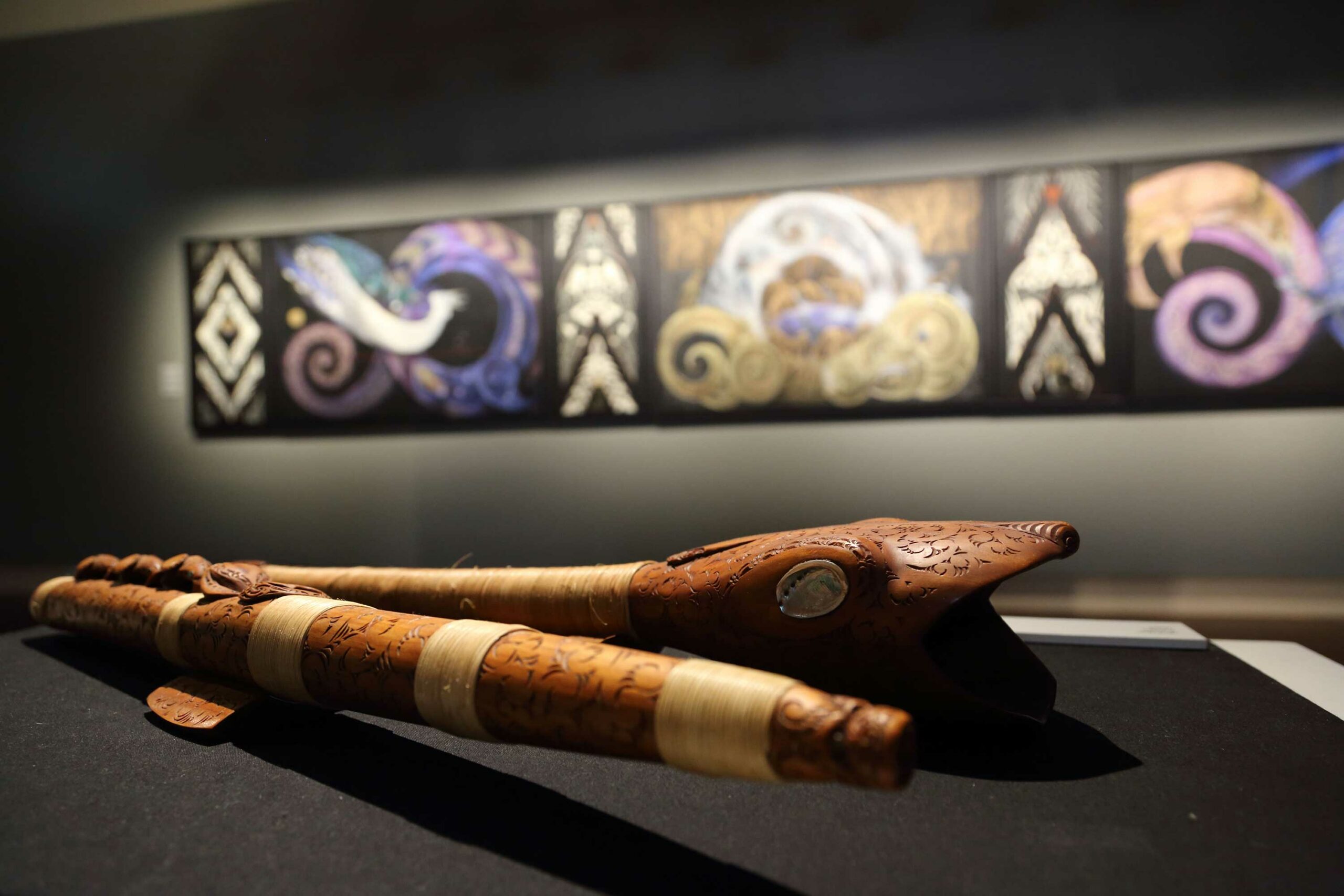 Two carved taonga pūoro and three paintings in a gallery