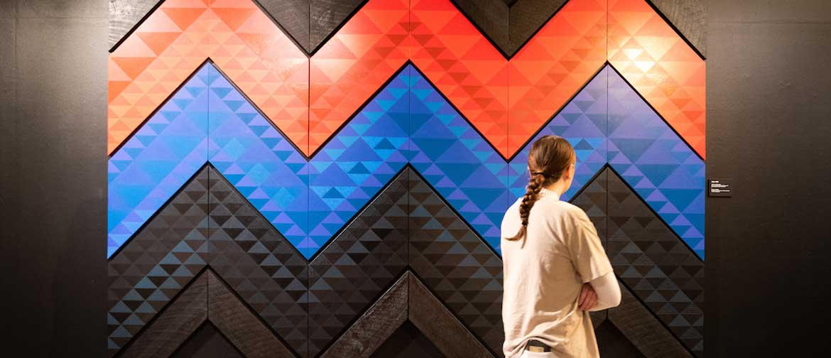 A woman looks at large panels of Māori art on a gallery wall