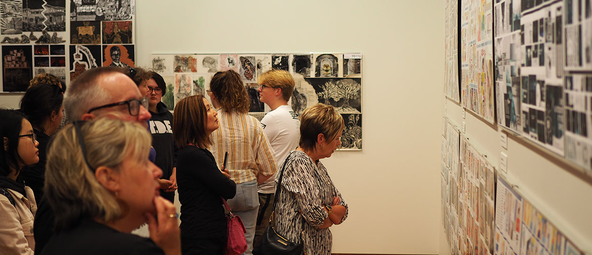A group of people view artworks on a gallery wall.