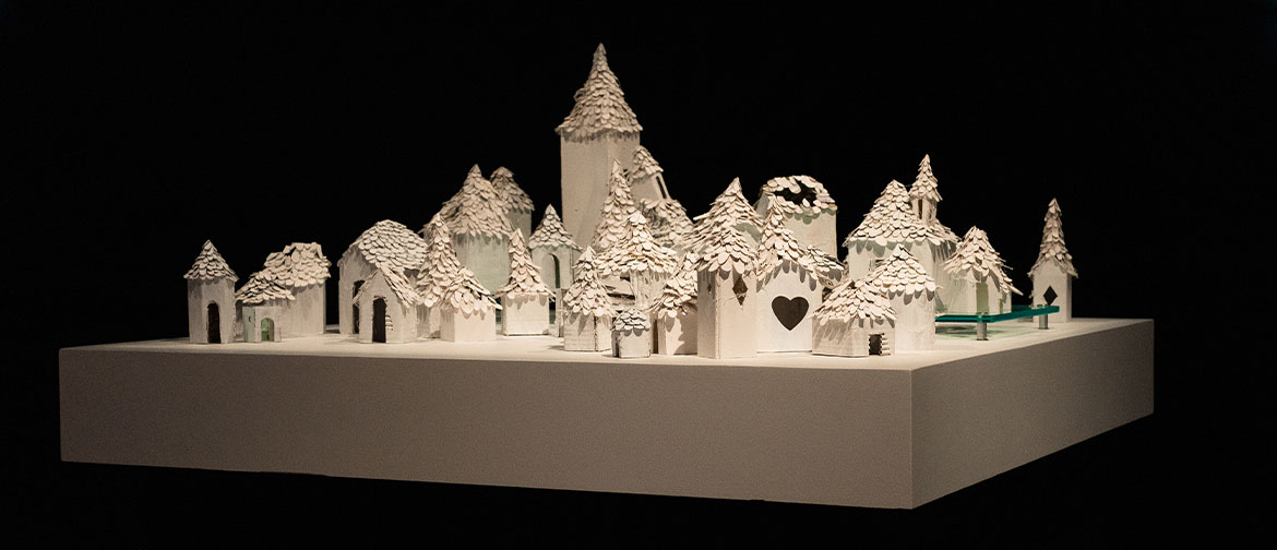A model town made from white card sits on a white plinth against a black background