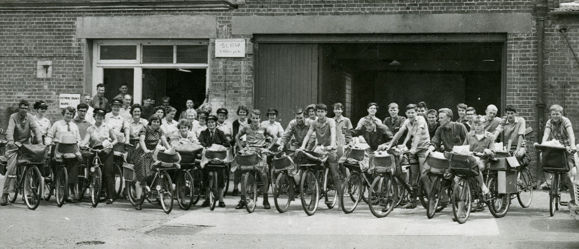 A black and white photo of many people on bicycles in a line outside a brick building.
