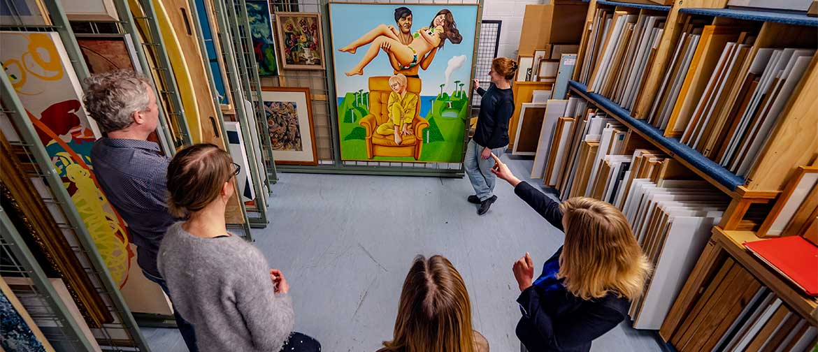 Five people looking at a painting inside an art storage area.