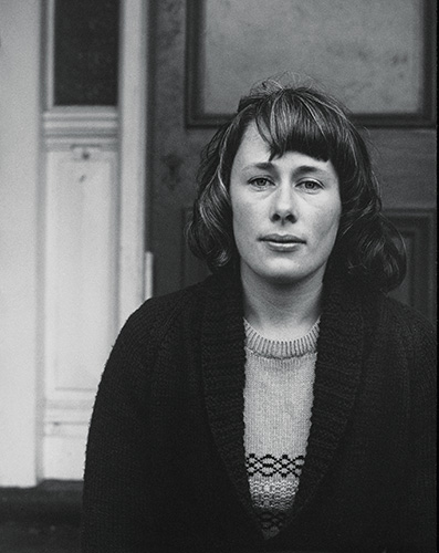 A black and white photo of a young woman sitting on the porch of an old house.