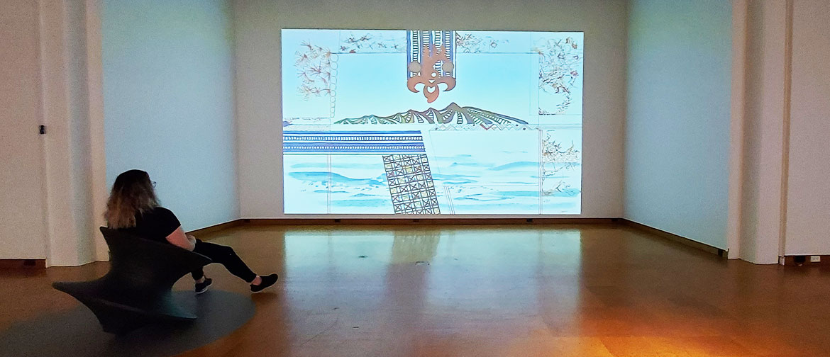A woman sits in front of a large projected image.